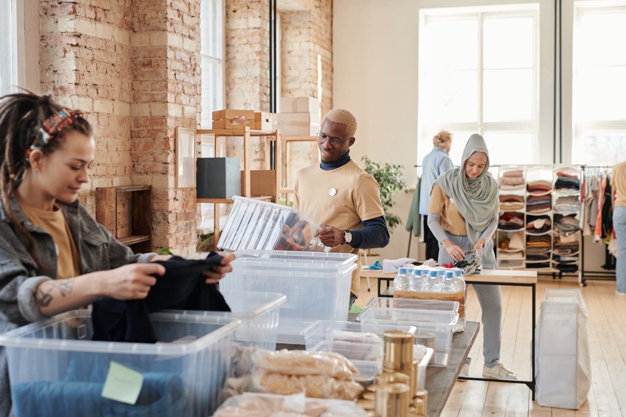 who-we-are Group of diverse volunteers organizing donated clothing and supplies in a bright, airy warehouse.